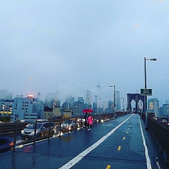 Brooklyn Bridge. I tusmørket på en diset novemberdag. Manhattan i baggrunden. Et par med paraply er ved at nå Brooklyn.
